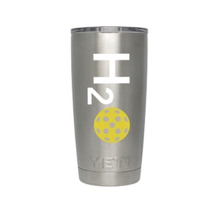 May include: A stainless steel tumbler with a white "H2" graphic and a yellow pickleball with gray dots. The tumbler has a silver lid and the brand name "YETI" is printed at the bottom.