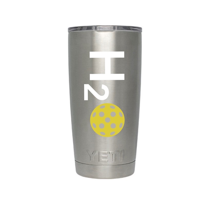 May include: A stainless steel tumbler with a white "H2" graphic and a yellow pickleball with gray dots. The tumbler has a silver lid and the brand name "YETI" is printed at the bottom.
