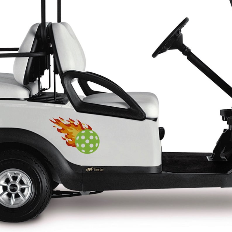 Puede incluir: Un carrito de golf blanco con un volante negro y asientos negros. Un pickleball verde y blanco con llamas est&aacute; en el lateral del carrito. El carrito tiene el texto "Club Car" en el lateral.