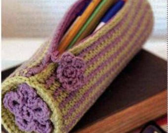 May include: A green and purple striped crocheted pencil case with a zipper closure and purple flower embellishments.