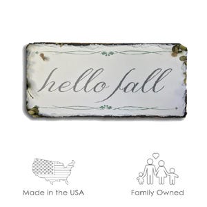 May include: A rustic wooden sign with a white background and the text "hello fall" in gray lettering. The sign has a distressed look and is decorated with green leaves and vines.