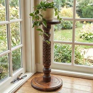 Sturdy wooden floor pedestal holding a large flower pot. Dark brown classic column made of solid oak or ash, designed as a stable display stand for ferns, bonsai, or indoor garden decor.