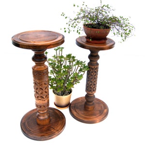 May include: Two wooden plant stands with intricate carvings. The stands are brown and have a round top and a round base. The stands are decorated with a floral pattern. The stands are perfect for displaying plants or other decorative items.