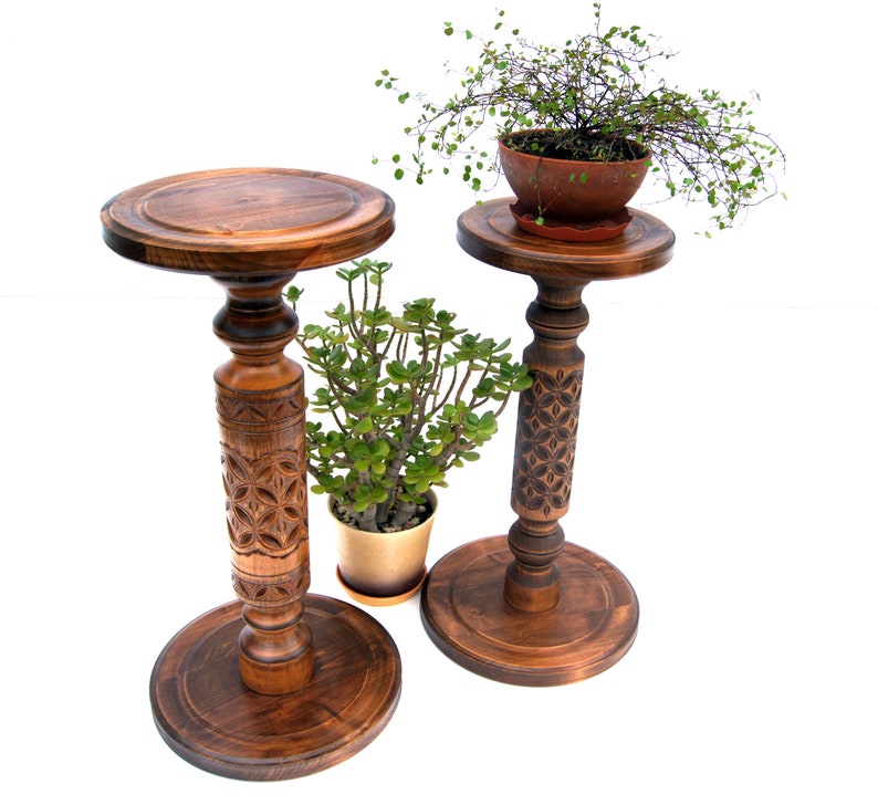 May include: Two wooden plant stands with intricate carvings. The stands are brown and have a round top and a round base. The stands are decorated with a floral pattern. The stands are perfect for displaying plants or other decorative items.