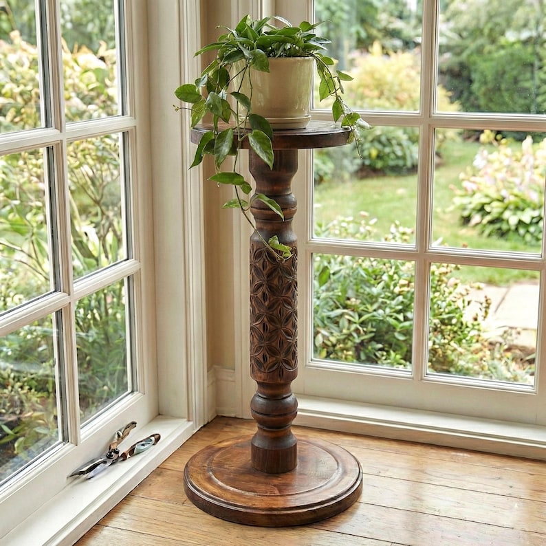 Sturdy wooden floor pedestal holding a large flower pot. Dark brown classic column made of solid oak or ash, designed as a stable display stand for ferns, bonsai, or indoor garden decor.