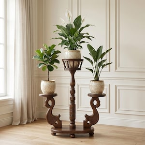 May include: A dark brown, three-tiered plant stand with three potted plants. The stand has ornate carvings and holds plants in speckled beige pots. The plants include a fiddle-leaf fig, a peace lily, and a bird of paradise plant.