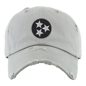 May include: A gray distressed baseball cap with a black and white embroidered patch of the state of Tennessee's symbol, three white stars in a circle.