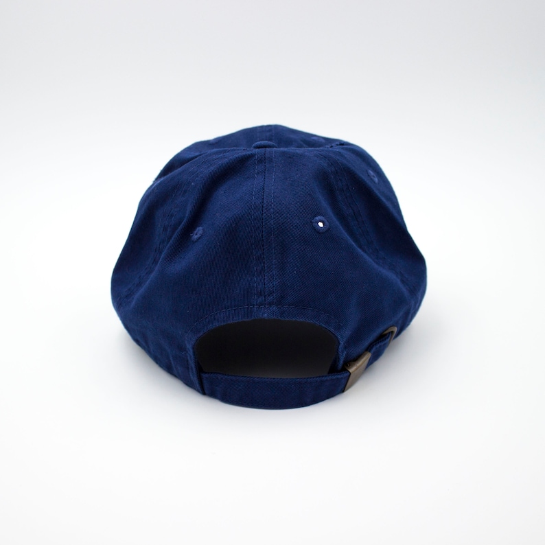 May include: A solid navy blue baseball cap with a brown adjustable strap in the back.