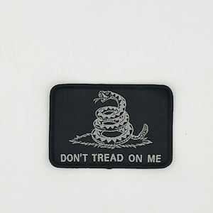 May include: A black embroidered patch with a silver-colored rattlesnake coiled and the text "DON'T TREAD ON ME".