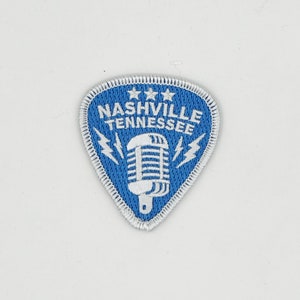 May include: A blue guitar pick shaped patch with white stitching. The patch features a white microphone with lightning bolts and the text "NASHVILLE TENNESSEE" with three white stars above the text.