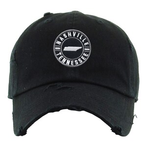 May include: Black distressed baseball cap with a white embroidered circle patch that says "Nashville Tennessee" and features a white outline of the state of Tennessee.