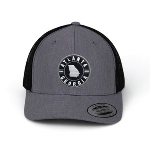 May include: A gray and black trucker hat with a white embroidered patch that says "Atlanta Georgia" and features an outline of the state of Georgia. The hat has a black mesh back.