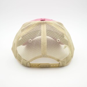 May include: A pink and beige mesh trucker hat with a plastic adjustable strap at the back.