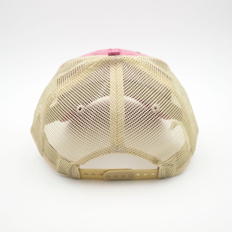 May include: A pink and beige mesh trucker hat with a plastic adjustable strap at the back.