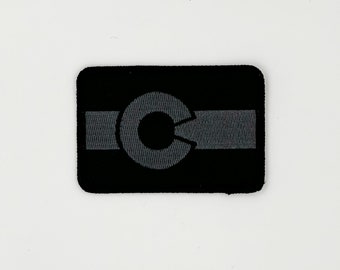 May include: Black and gray embroidered patch with a stylized letter "C" in the center. The letter is surrounded by a gray band.