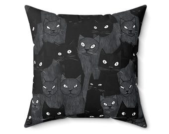 May include: Square throw pillow with a repeating pattern of black cat faces on a dark gray background. The cats have white eyes and are in various poses. The pillow is a decorative item.