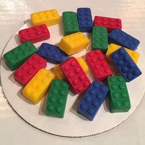 May include: A collection of colorful plastic toy bricks in red, yellow, blue, and green. The bricks are arranged on a white surface.