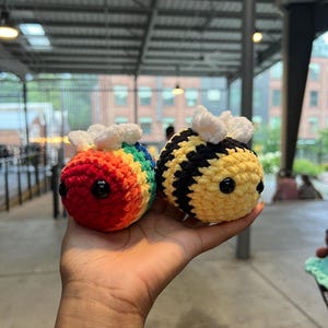 Può includere: Due api fatte a mano all'uncinetto. Un'ape è color arcobaleno, l'altra è gialla e nera. Entrambe hanno ali bianche e soffici e occhi neri a bottone. Queste fantasiose api amigurumi sono perfette per un giocattolo per bambini o un regalo unico.