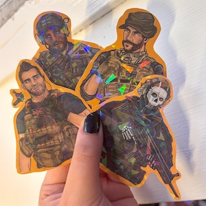 May include: Four holographic stickers featuring illustrations of characters from a video game. The stickers have an orange border and depict soldiers in military gear. One character wears a skull mask, and another has a mustache and a hat.