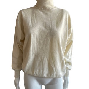 Könnte beinhalten: Ein cremefarbener Rollkragenpullover mit langen Ärmeln. Der Pullover ist aus weichem, gestricktem Stoff.