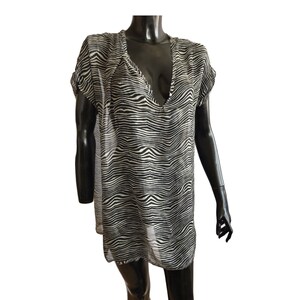 Può includere: Una tunica trasparente con stampa zebrata in bianco e nero, scollo a V e maniche corte.