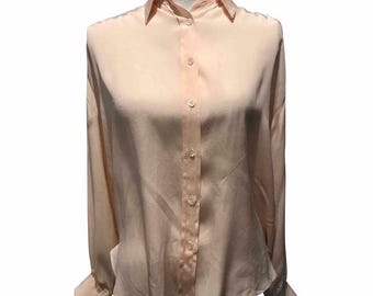 May include: A light peach-colored button-down shirt with long sleeves. The shirt has a classic collar and button closures down the front. The fabric appears to be a smooth, silky material. The sleeves have buttoned cuffs.