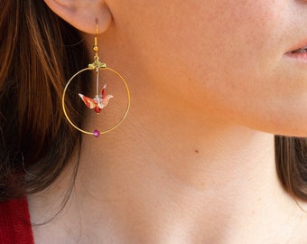May include: Gold hoop earrings with a red and white origami crane hanging from the hoop. A small purple crystal dangles from the bottom of the hoop.