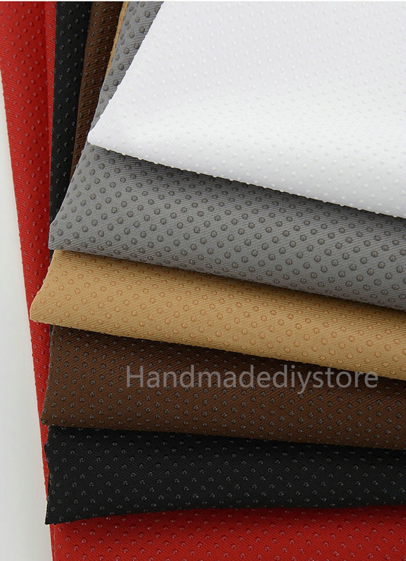May include: A stack of seven fabric swatches in various colors, including red, black, brown, beige, gray, and white. The fabric has a textured, dotted pattern.