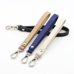 May include: Three leather keychains with silver swivel clips. The keychains are beige, navy blue, and cream.