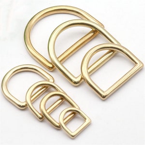 Op de afbeelding: Set van zes goudkleurige metalen D-ringen in verschillende maten. De ringen zijn glad en hebben een gepolijste afwerking.