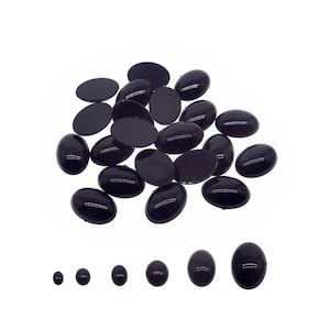 May include: A pile of black oval-shaped plastic cabochons, some larger than others, on a white background.