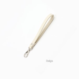May include: A beige leather strap with a silver swivel clasp. The strap is about 12 inches long.