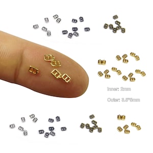 Könnte beinhalten: Sortiment kleiner Metallschnallen in Gold, Silber und Schwarz. Die Schnallen sind etwa 3,5 x 5 mm groß mit einer Innenmaße von 2 mm.