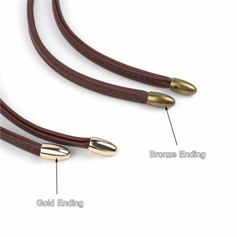 May include: Two brown leather cords with gold and bronze bullet-shaped ends. The cord on top has a bronze end, and the cord on the bottom has a gold end. The ends are labeled "Bronze Ending" and "Gold Ending".