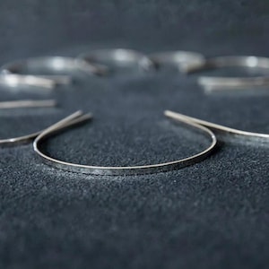 May include: A silver hammered bangle bracelet. The bracelet is thin and delicate, with a smooth, polished finish.