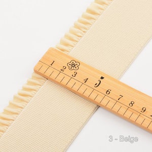 May include: Beige elastic trim with a ruffled edge. The trim is measured with a ruler showing 5 inches.
