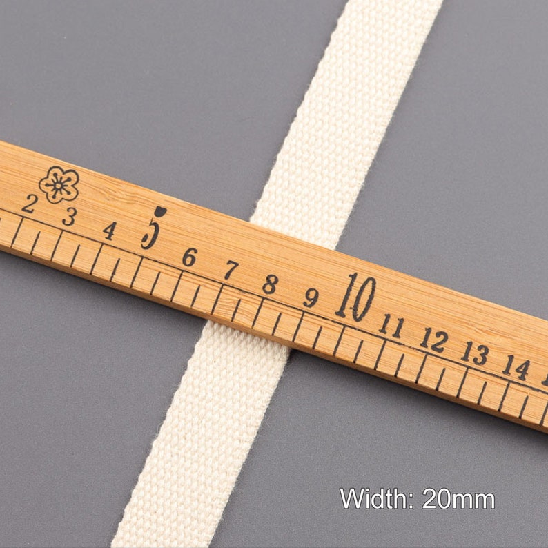 May include: A close-up of a white cotton webbing measuring 20mm wide. The webbing is laid on top of a wooden ruler with markings in millimeters.