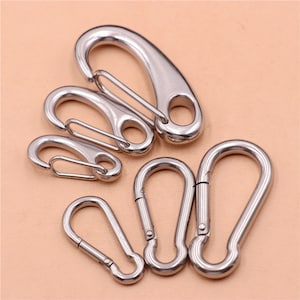 May include: A set of six silver metal snap hooks of varying sizes. The hooks are all made of the same material and have a smooth, polished finish.