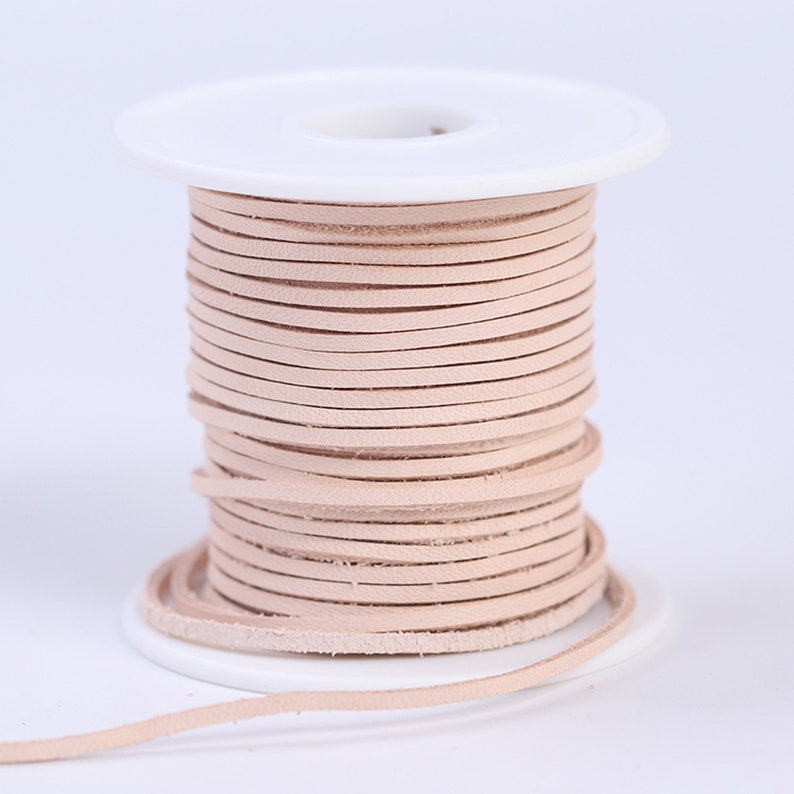 May include: A spool of light pink leather cord, wound around a white plastic spool. The cord is thin and flat, and it is perfect for crafting projects.