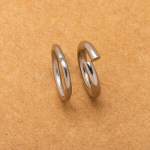 May include: Two silver jump rings, one with a small gap, on a brown surface.