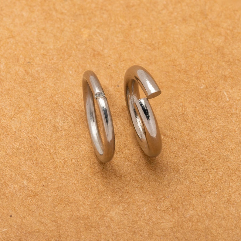 May include: Two silver jump rings, one with a small gap, on a brown surface.