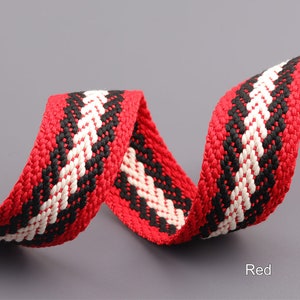 Pode incluir: Cinta de algod&atilde;o tecida em listras vermelhas, brancas e pretas. A cinta est&aacute; torcida e dobrada, mostrando as diferentes cores e padr&otilde;es.