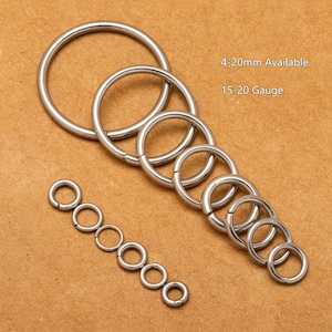May include: Assortment of silver metal jump rings in various sizes, ranging from 4 to 20 mm in diameter. The text "4-20mm Available 15-20 Gauge" is printed on a brown background.
