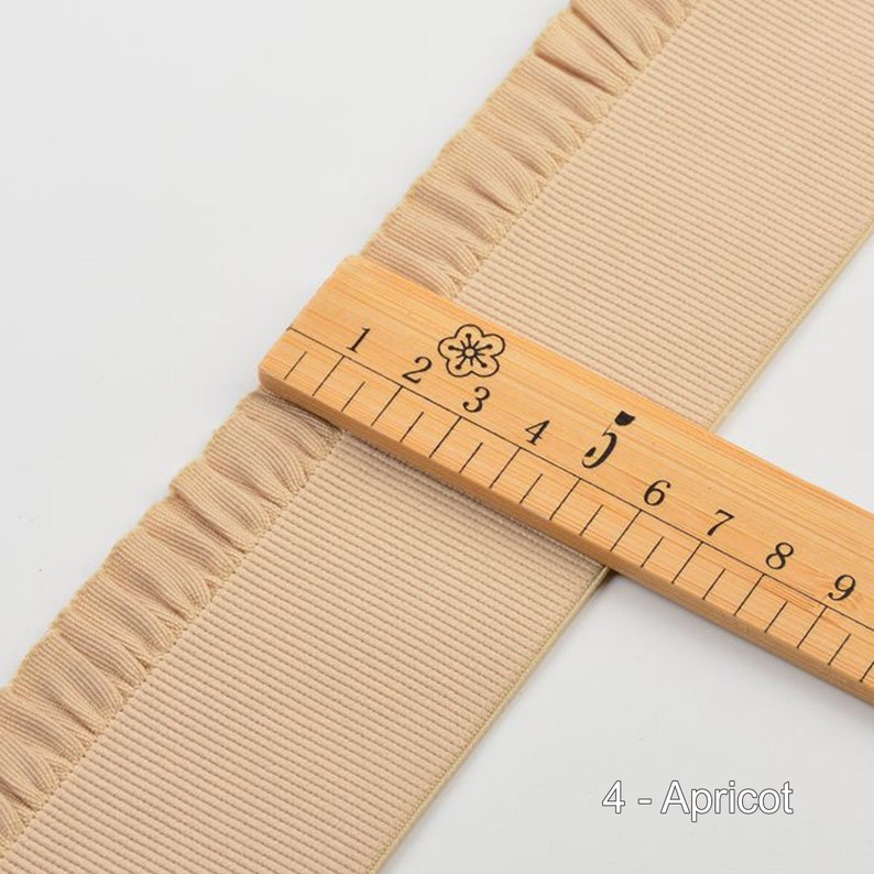 May include: A close-up of a beige ruffled trim with a wooden ruler measuring 5 inches. The trim is labeled "4 - Apricot".
