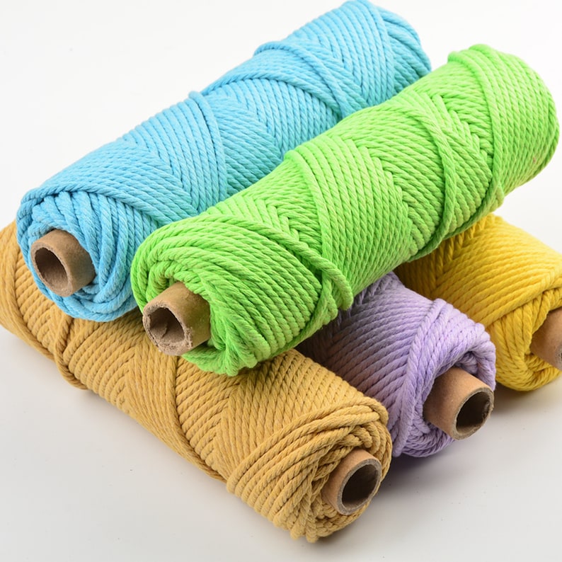 May include: Four spools of cotton rope in different colors: light blue, green, purple, and yellow. The spools are stacked on top of each other.