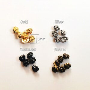 Może przedstawiać: Zestaw metalowych guzików w kształcie róży w kolorze złotym, srebrnym, brązowym i stalowym. Każdy guzik ma średnicę 5 mm.