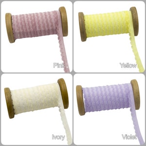 May include: Four spools of elastic trim with a scalloped edge. The trim is in four colors: pink, yellow, ivory, and violet.