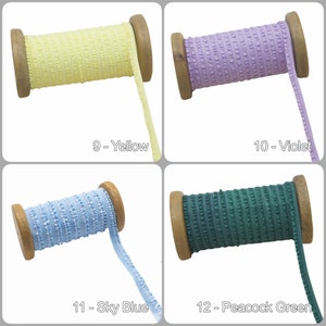 May include: Four spools of ruffled trim in yellow, violet, sky blue, and peacock green. Each spool is made of wood and has a label with a number and colour name.
