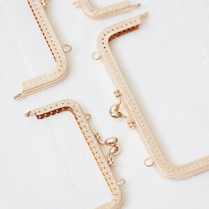 May include: Four gold-toned metal purse frames with intricate designs. The frames are open and ready to be used for a DIY project.