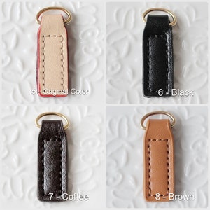 Op de afbeelding: Vier leren sleutelhangers in verschillende kleuren: origineel, zwart, koffie en bruin. Elke sleutelhanger heeft een goudkleurige ring en is gemarkeerd met een nummer en kleurnaam. De sleutelhangers zijn rechthoekig met gestikte randen.